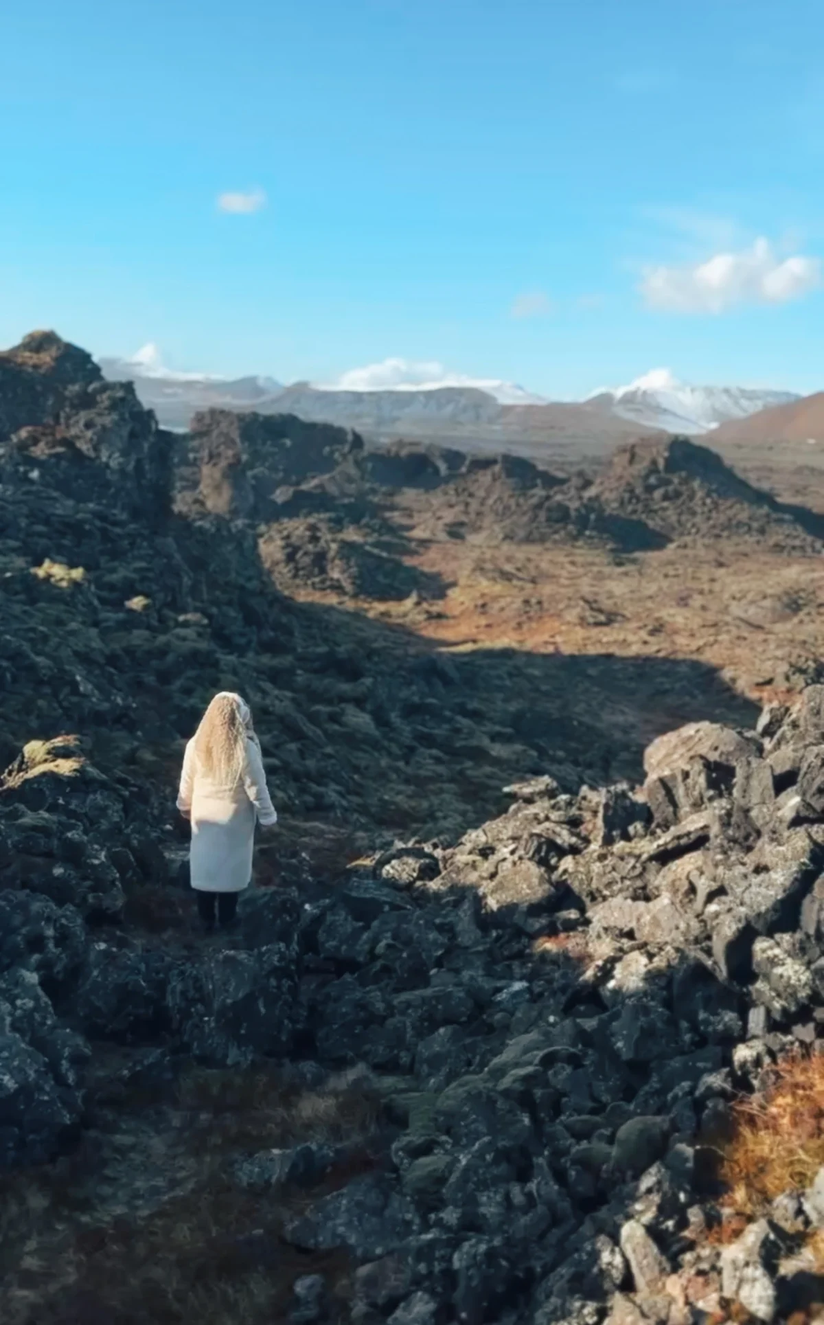 Woman in a white coat in a field of old lava