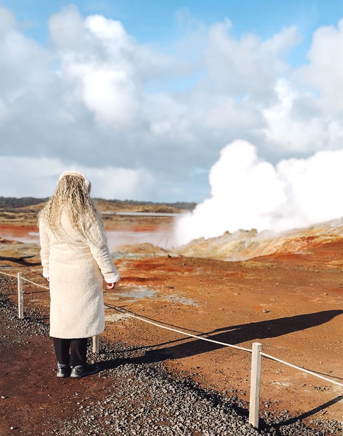 Woman in a white coat looking at the Gunnuhver Hot Springs in Iceland