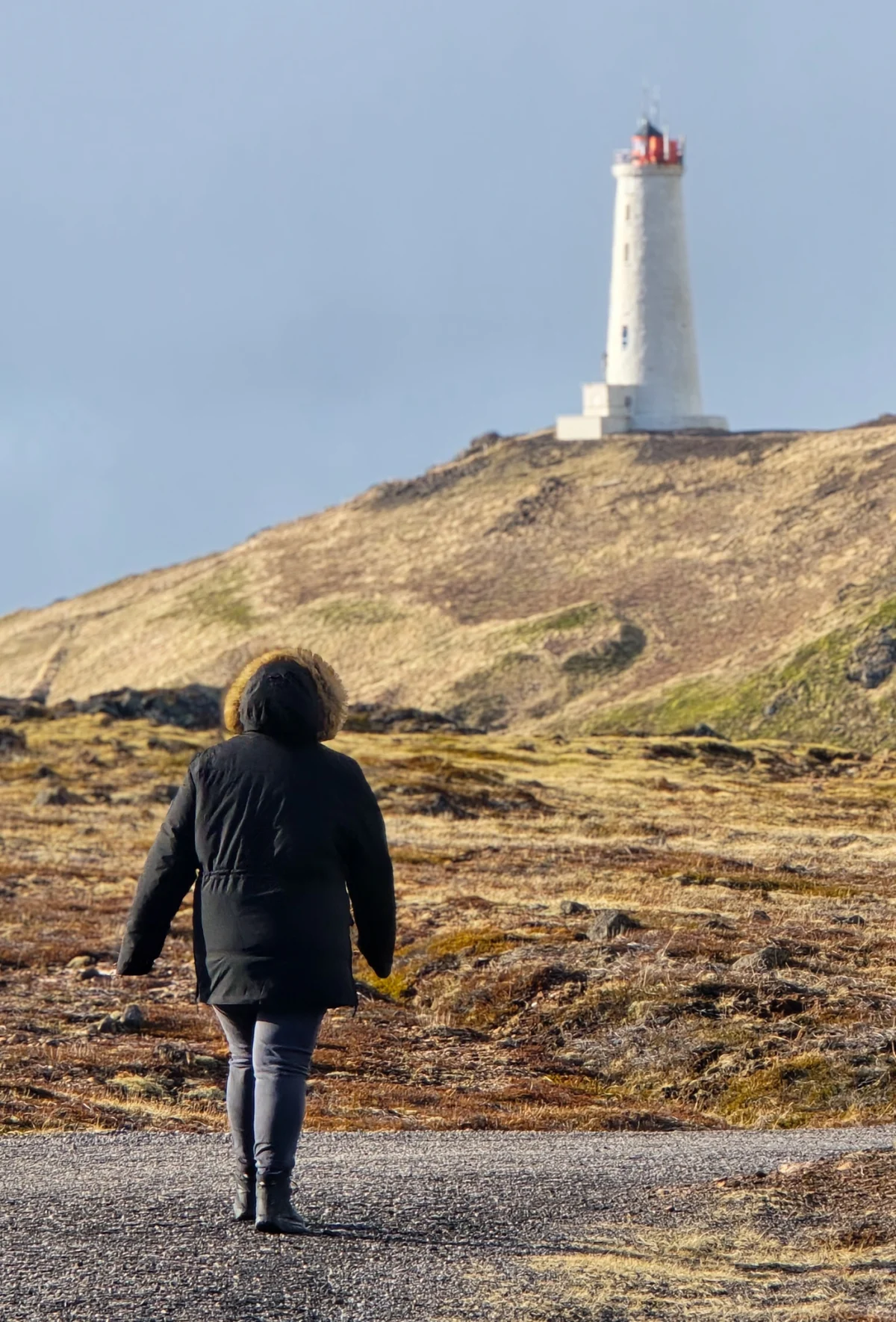 Woman in a jacket looking at the oldest lighthouse in Iceland